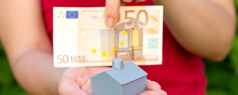 Personne présentant un billet de 50 euros derrière un modèle réduit de maison