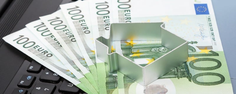 Emporte pièce en forme de maison sur un tapis de billets de 100 euros.