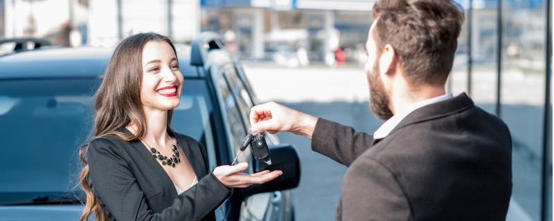Cliente d'un concessionnaire automobile recevant les clés de sa nouvelle voiture devant celle-ci