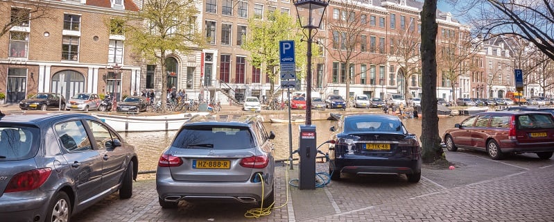 Vue sur une rue au bord des quais d'Amsterdam avec plusieurs voitures garées.