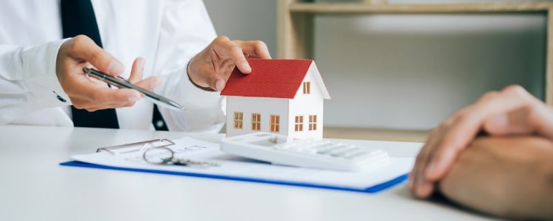 Un agent immobilier et un client discutent devant un contrat sur lequel se trouve un modèle réduit de maison.