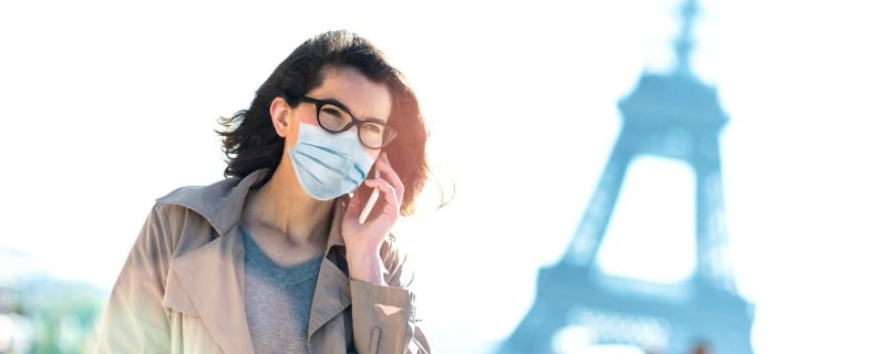 Femme marchant dans paris avec un masque sur le visage et la tour eiffel floue en arrière plan