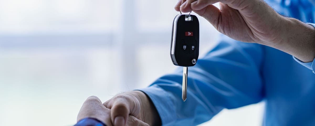  Un vendeur remet les clés d'une voiture à un acheteur après une poignée de main, illustrant un achat ou une transaction.