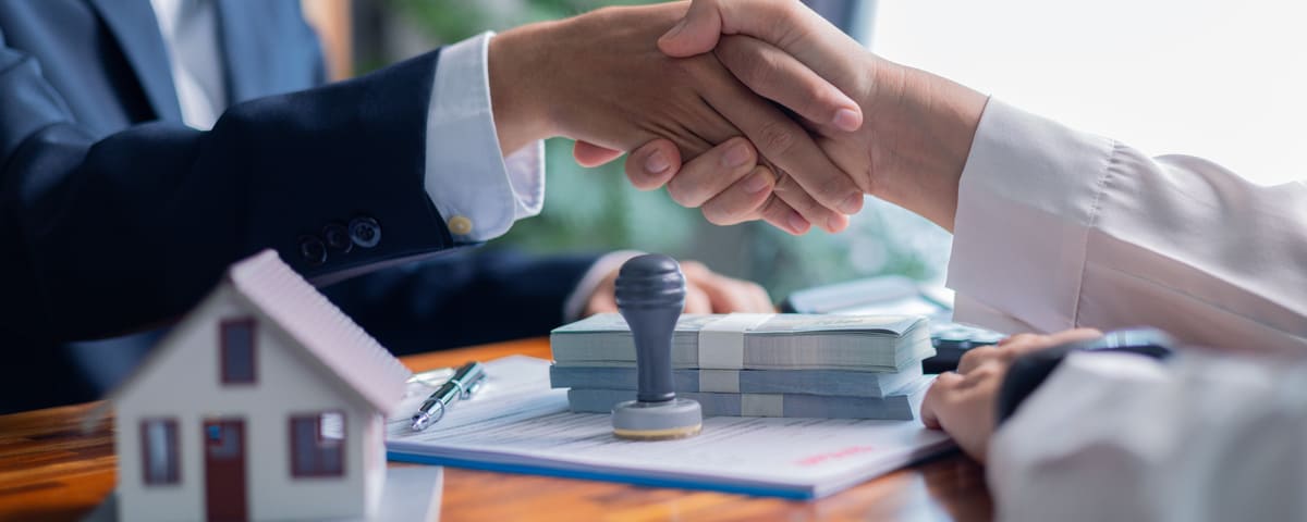 Deux personnes se serrent la main par-dessus un contrat, avec une petite maison modèle