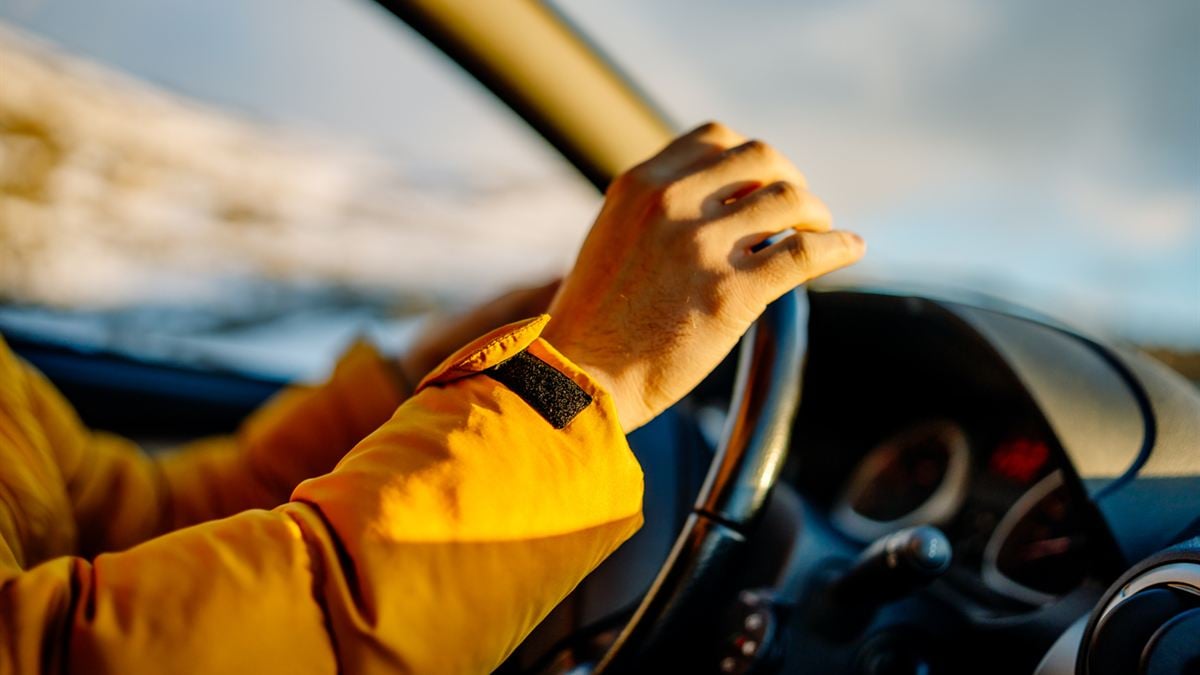 Défaut d'assurance auto : la main d'un conducteur en blouson jaune posée sur le volant, au soleil couchant