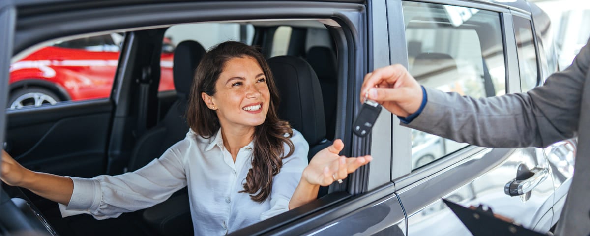 Femme heureuse recevant les cl&eacute;s de voiture chez le concessionnaire
