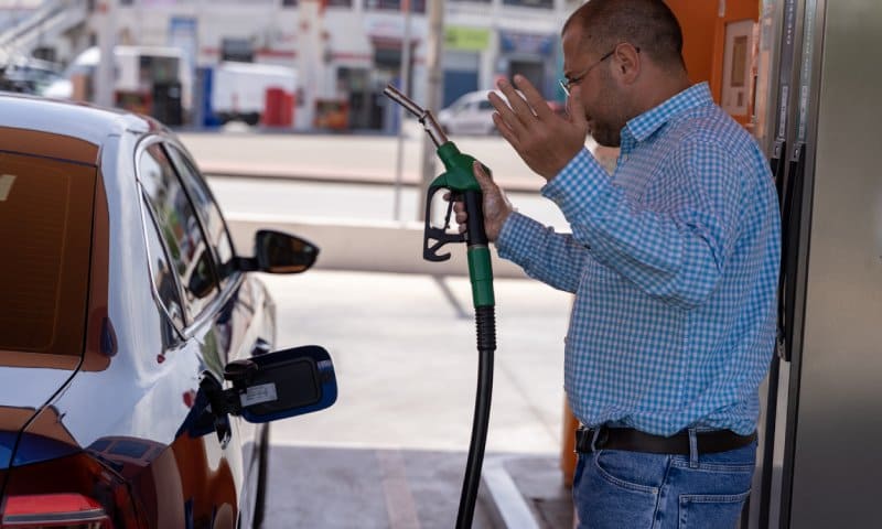 Homme confus à la station-service tenant la buse de carburant près de la voiture